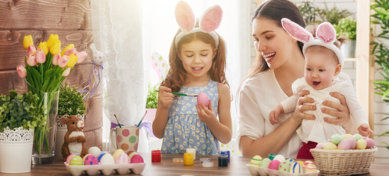 Happy mother and children colouring eggs for Easter